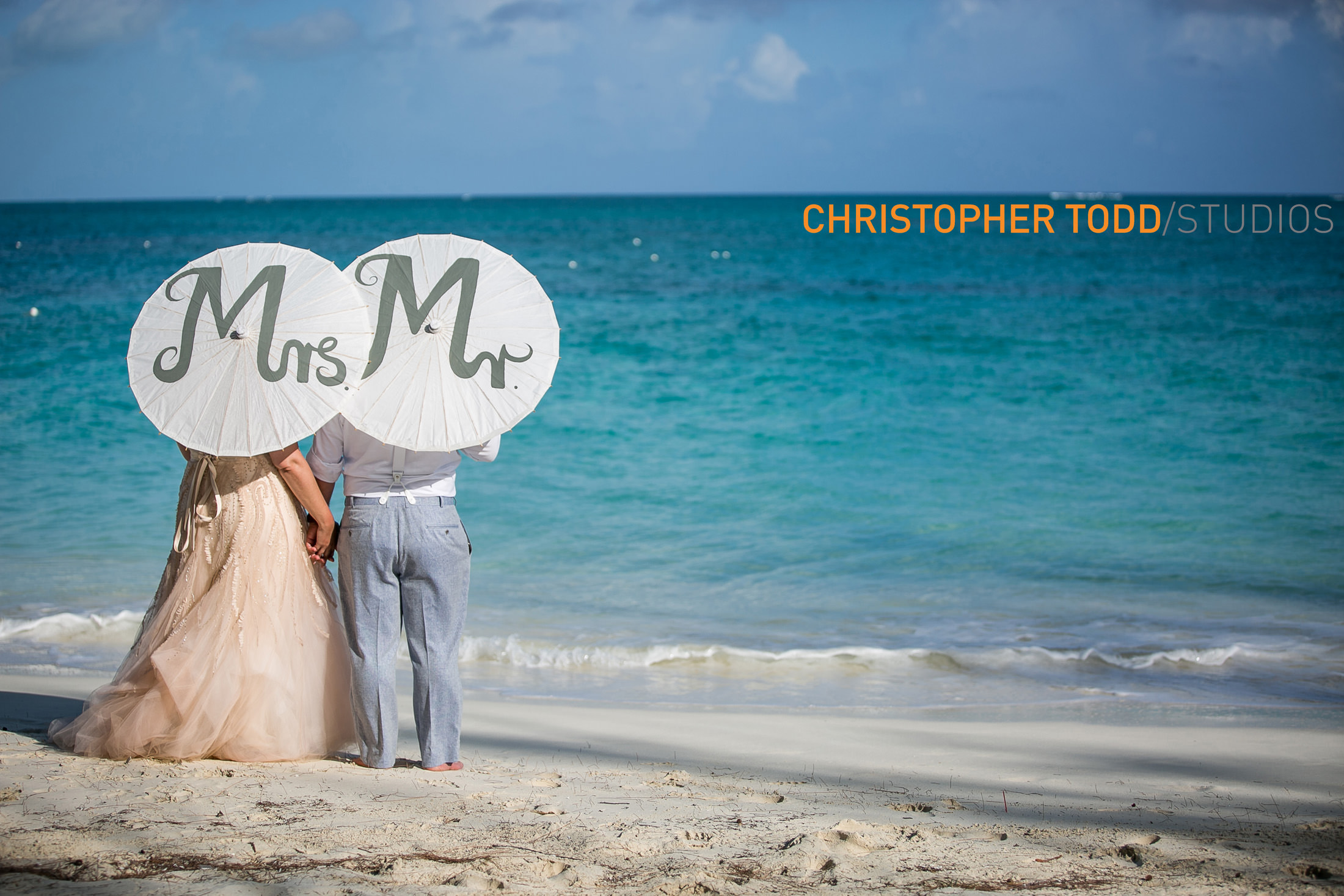 bride and groom elopement photo staring at blue ocean holding mr and mrs. umbrellas