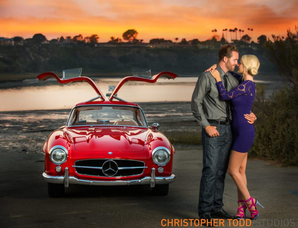 couple embracing in front of vintage red car during sunset at Newport Back Bay