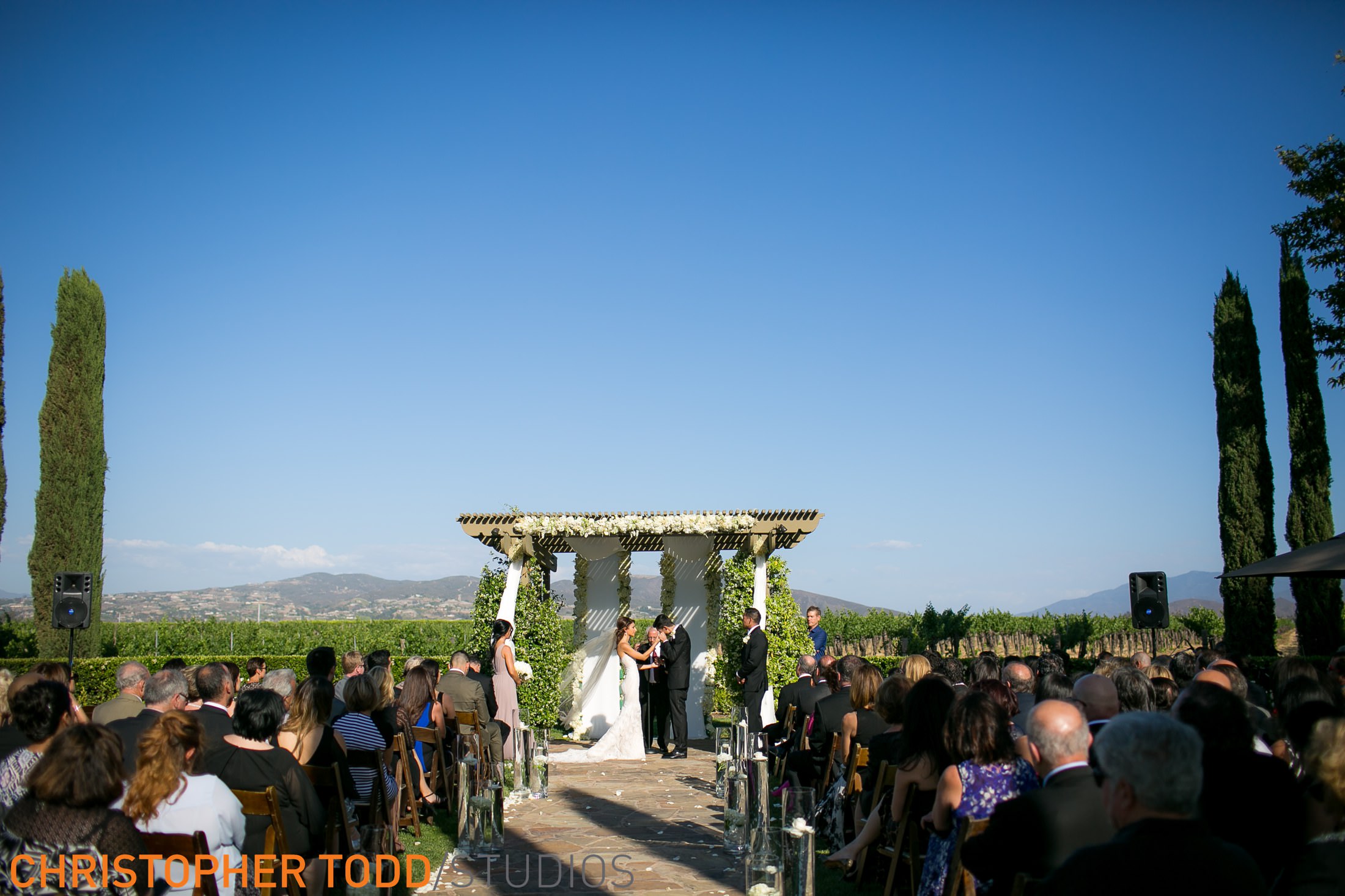image looking down aisle at arch where bride and groom stand exchanging vows at ponte winery temecula.