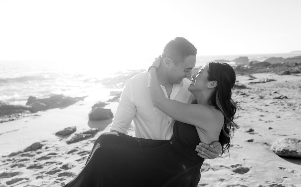 black and white photo of guy holding fiancé in his arms on beach