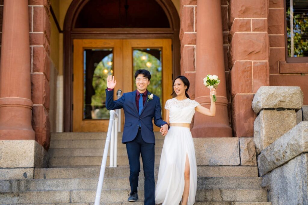 bride and groom walking out of Old Orange County Courthouse holding hands up just married