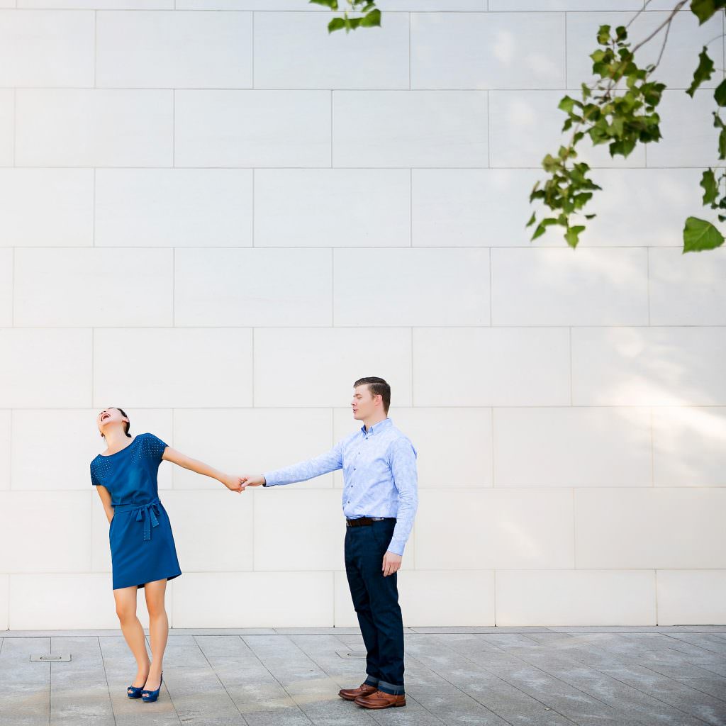couple holding hands in front of white brick wall