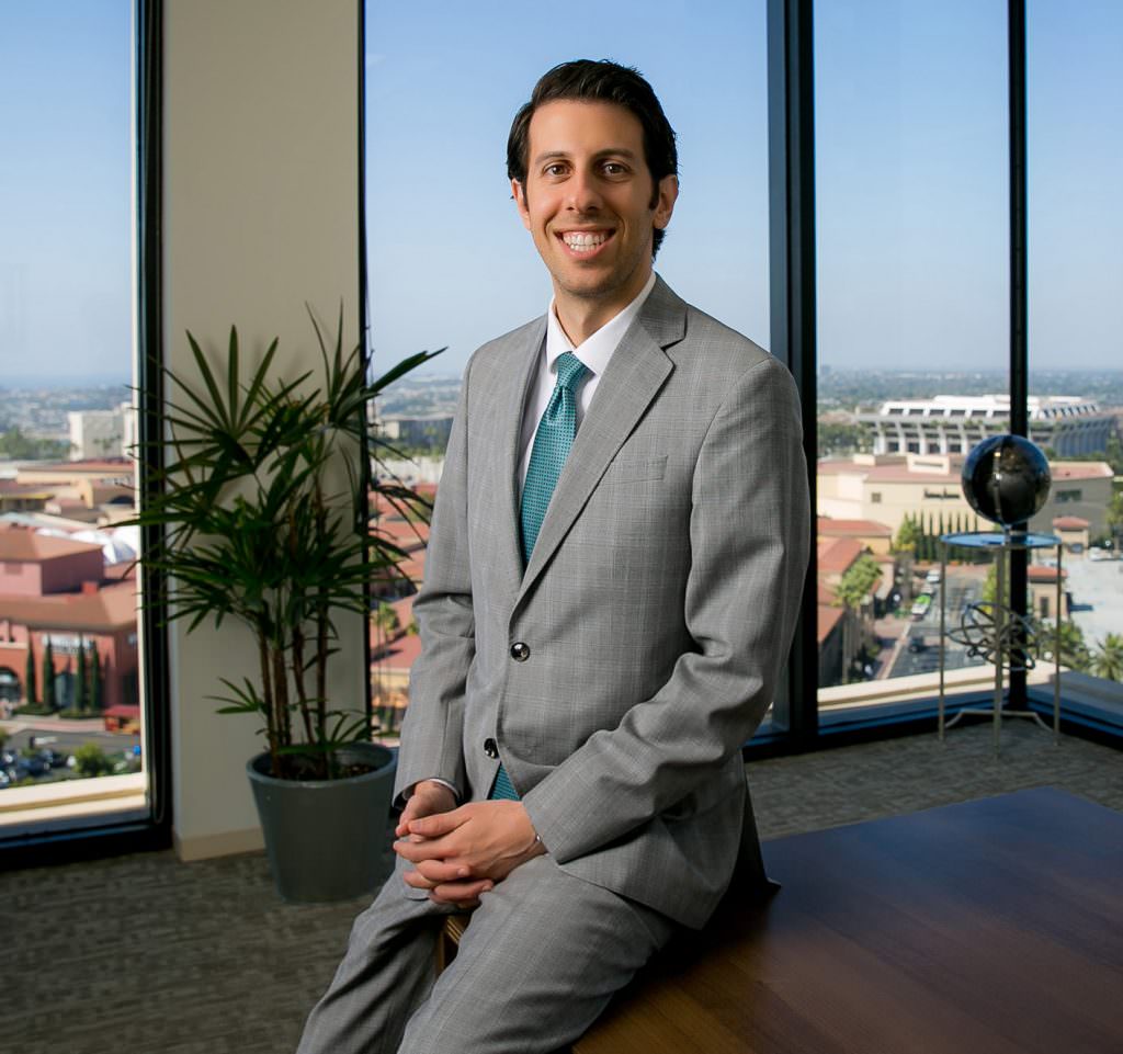 corporate executive headshot in orange county of mad wearing grey suit sitting in office.