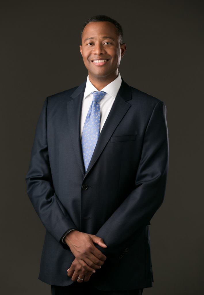 Example of doctor headshot wearing a suit on dark grey backdrop.