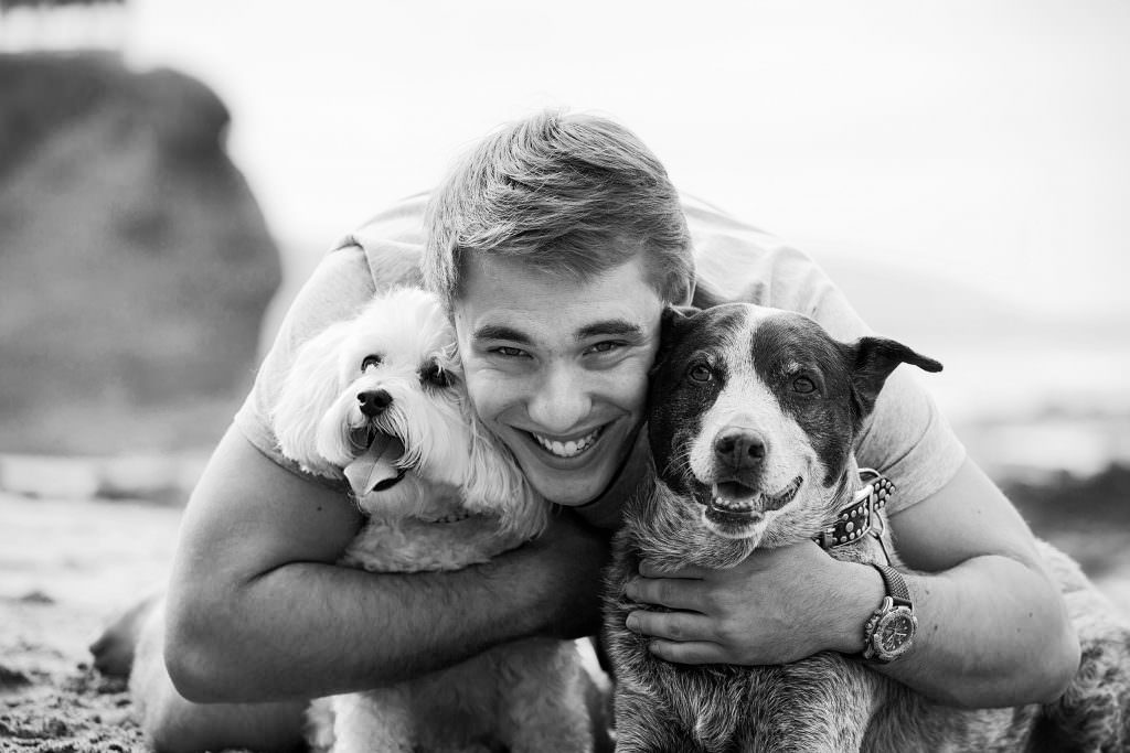 teenage boy hugging to dogs on beach