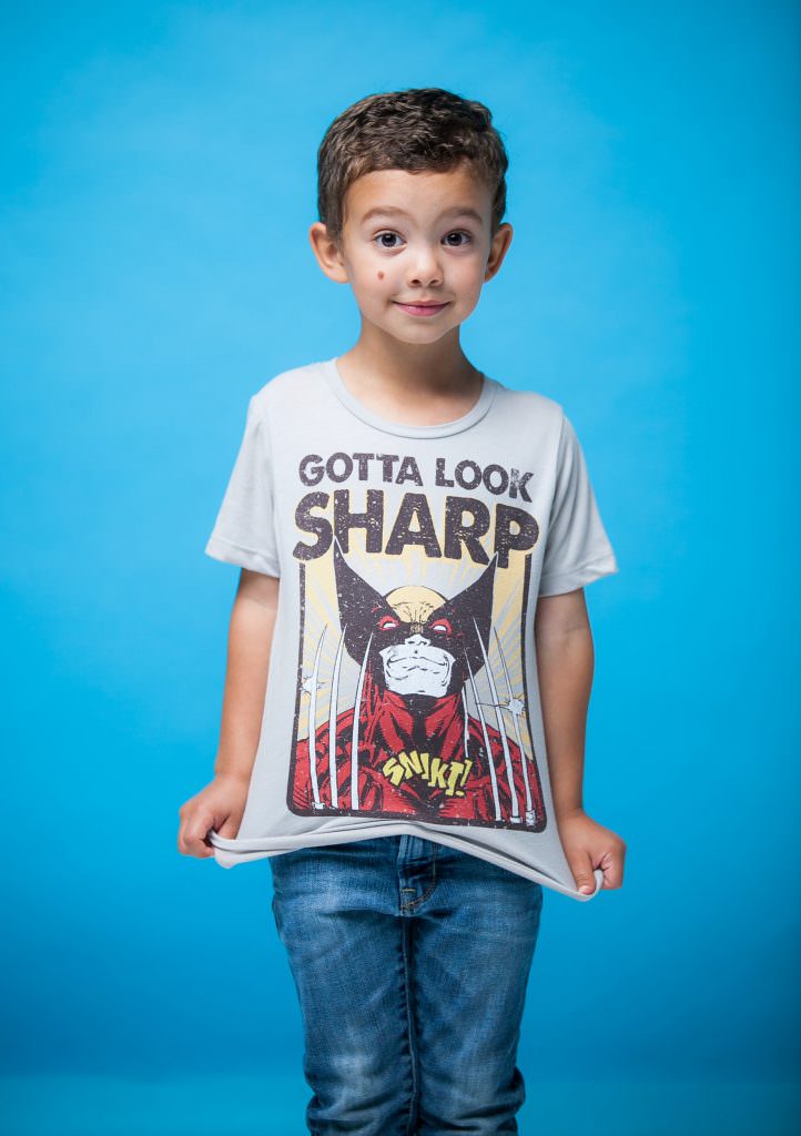 Kindergarten boy wearing superhero shirt posing with blue backdrop.
