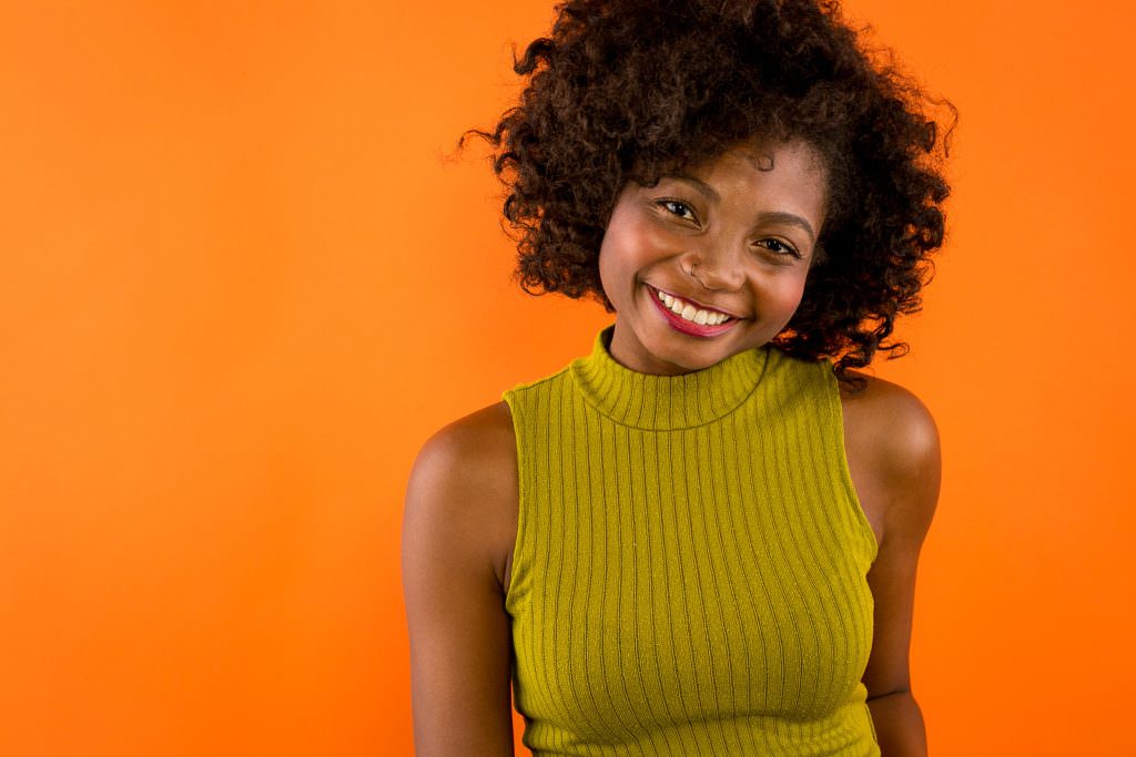 Female black model headshot on orange backdrop.