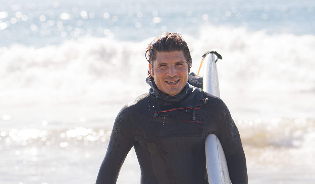 man in wetsuit carrying surfboard after getting out of the water