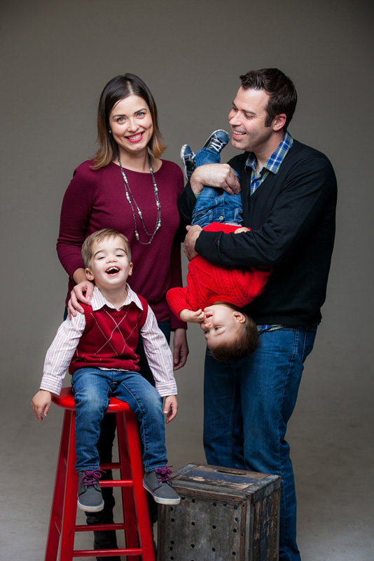 Playful young family in photo studio with grey backdrop.