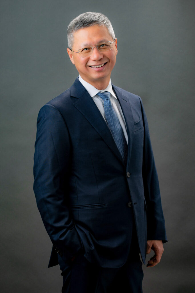 Asian male wearing suit in front of grey backdrop for headshot photo