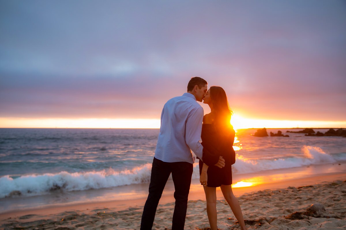 couple kissing on beach during sunset after surprise marriage proposal