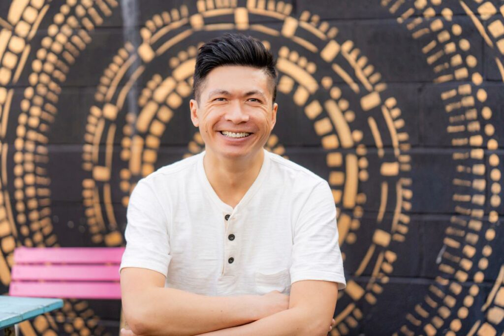 Young asian male wearing white shirt posing in front of Muriel for professional dating profile photos.