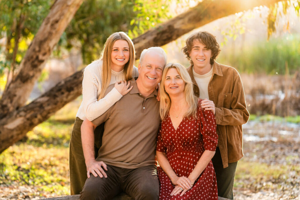 family with earth tone color scheme posing for family portraits with tree in background