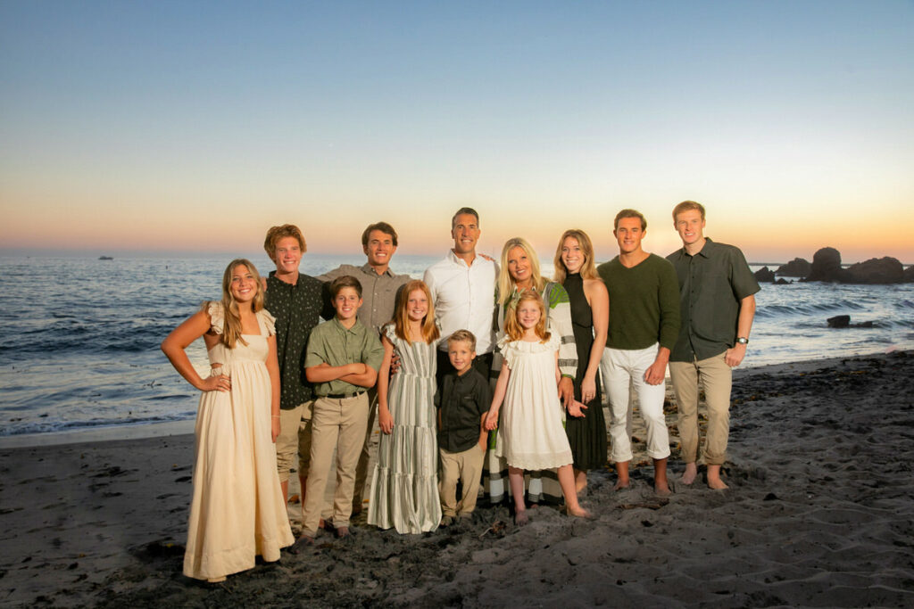 Sunset family photo of mom and dad and ten children posing on the beach for photoshoot