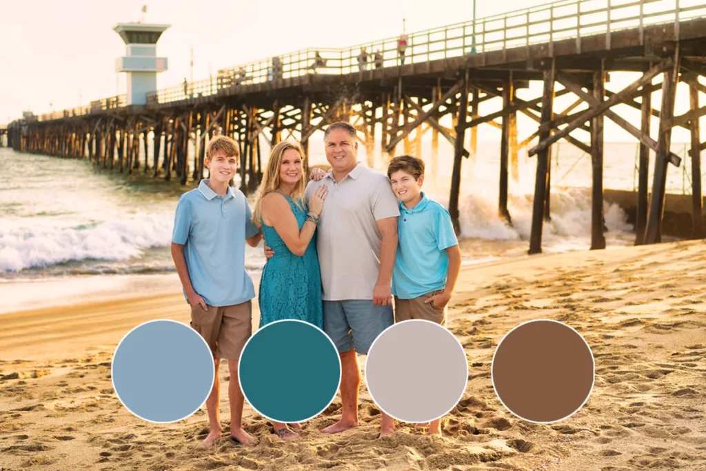 Family of four wearing shades of blue standing in front of pier at beach.