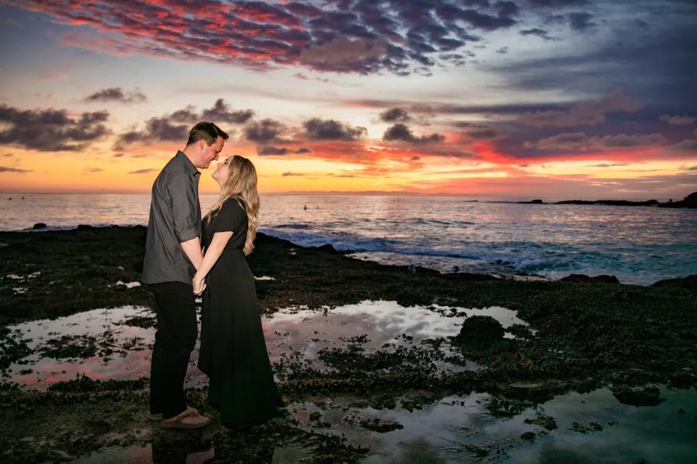 couple wearing black standing on tide pools during dramatic sunset