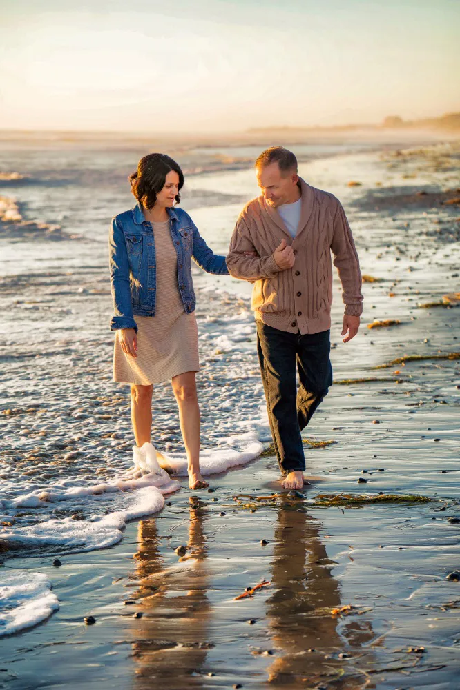 Older couple holding hands walking in low tide wearing cardigan sweater