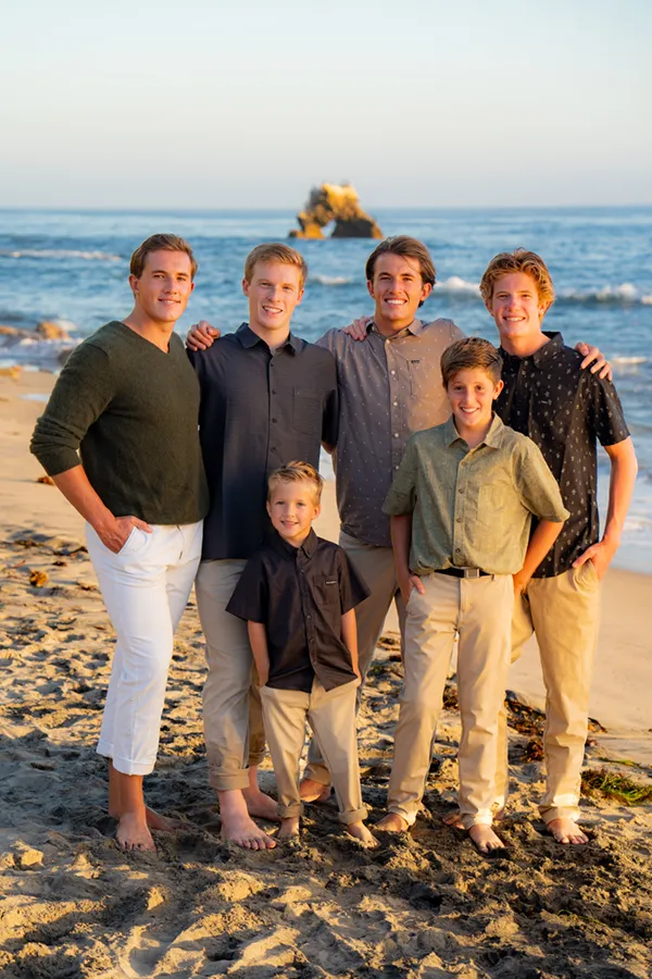 brothers wearing khakis and white pants standing on the beach posing for beach photoshoot