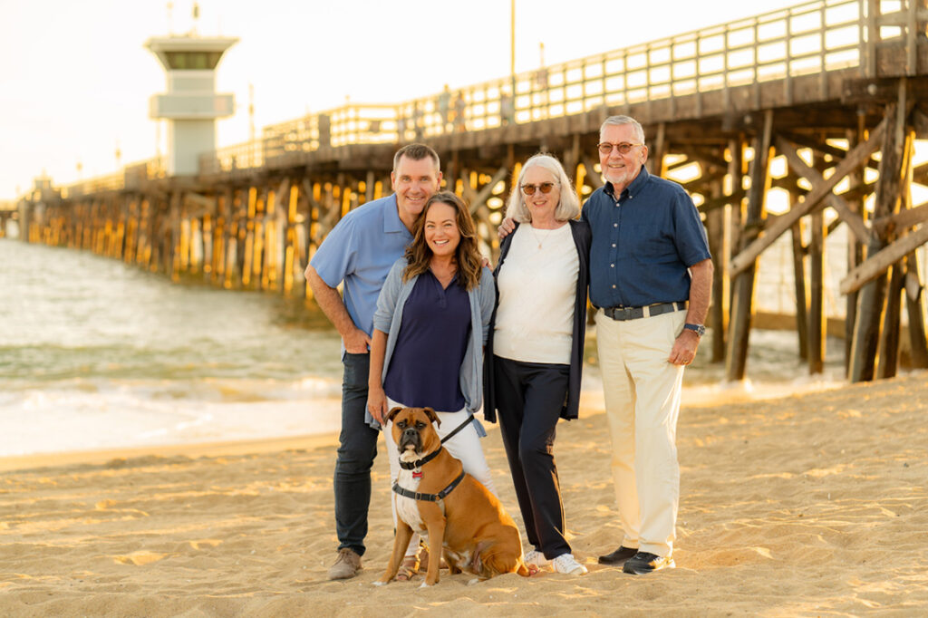 Four adults with dog standing on sand in front of Balboa Pier