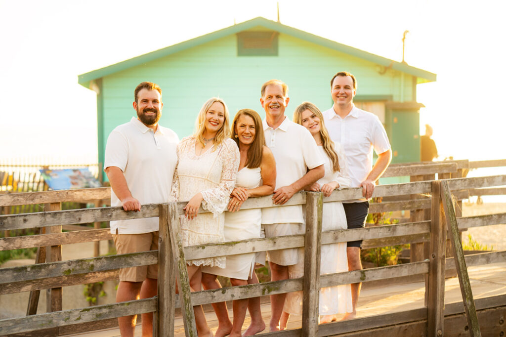 6 adults wearing light color outfits with crystal cove cottage behind them