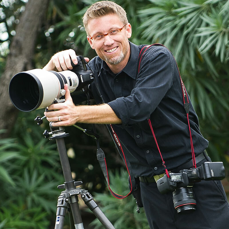 event photographer stands with camera on tripos waering all black